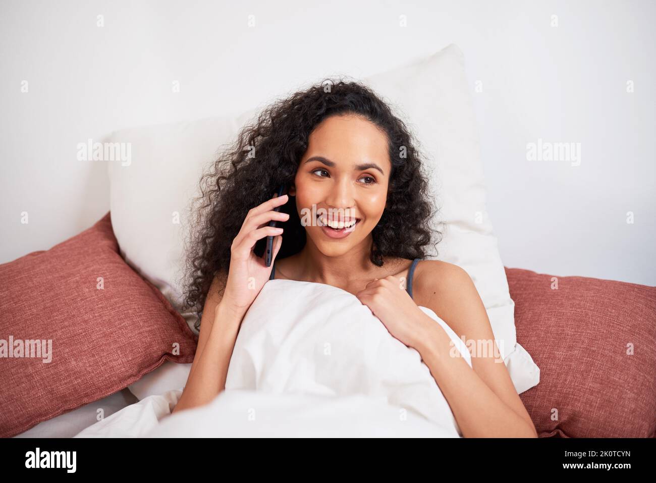 Nahaufnahme einer jungen, multiethnischen Frau, die sich mit Kissen im Bett mit dem Handy unterhielt Stockfoto