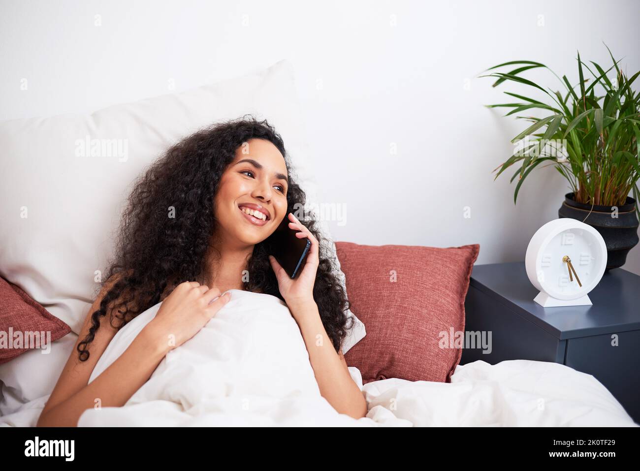 Eine junge, multiethnische Frau lacht während eines intimen Fernanrufs vom Bett aus Stockfoto