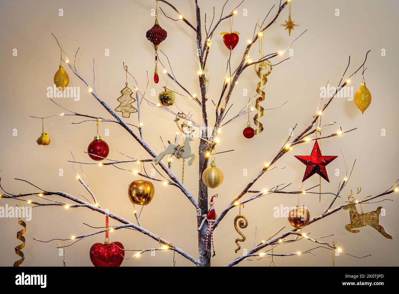 Weihnachtsbaumschmuck in traditionellem Rot und Gold hängt an einem modernen Zweig mit Schnee-Effekt Stockfoto