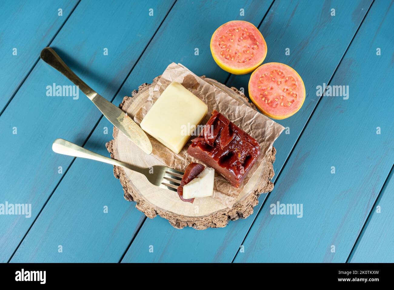 Goldene Gabel mit Stücken von Guava süß mit Käse auf einem Holzteller, neben einem Messer und einem Guava. Stockfoto