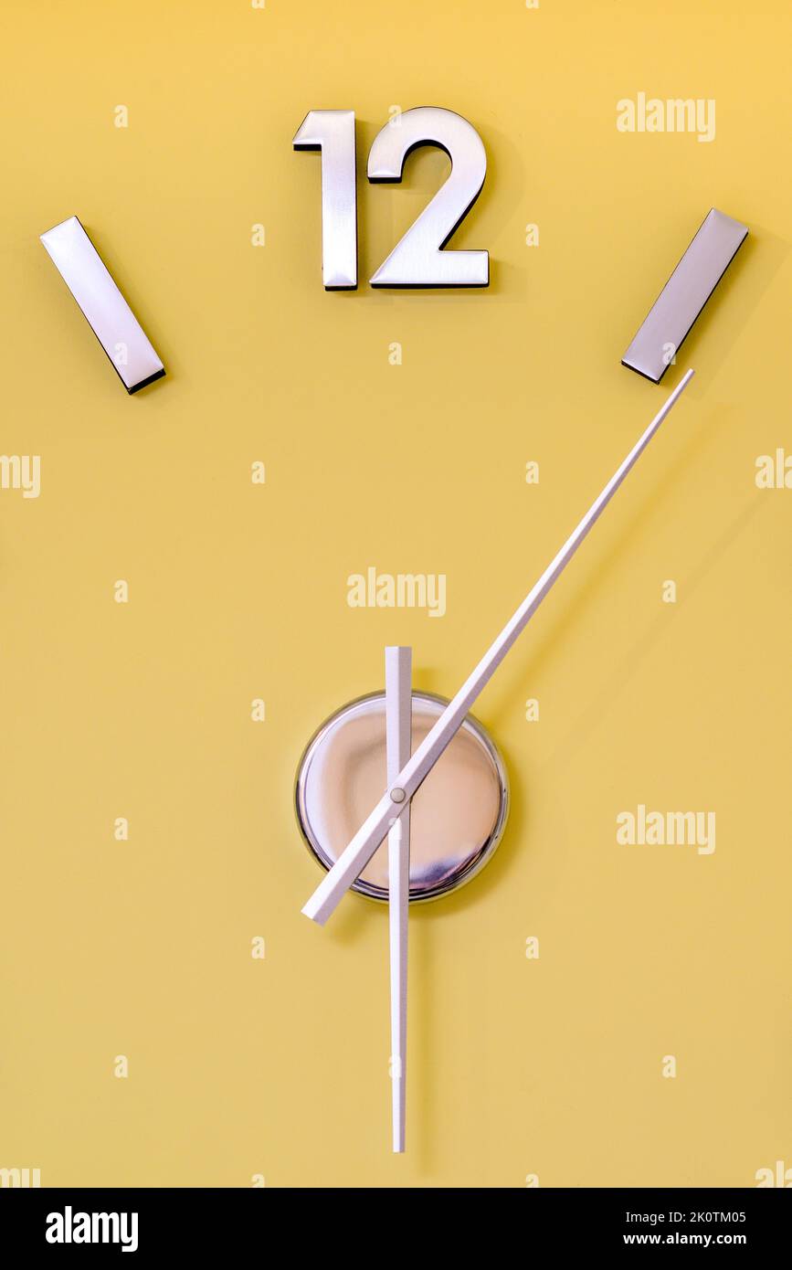 Silberne Chrom-Uhr mit der Nummer 12 an einer gelben Wand Stockfoto