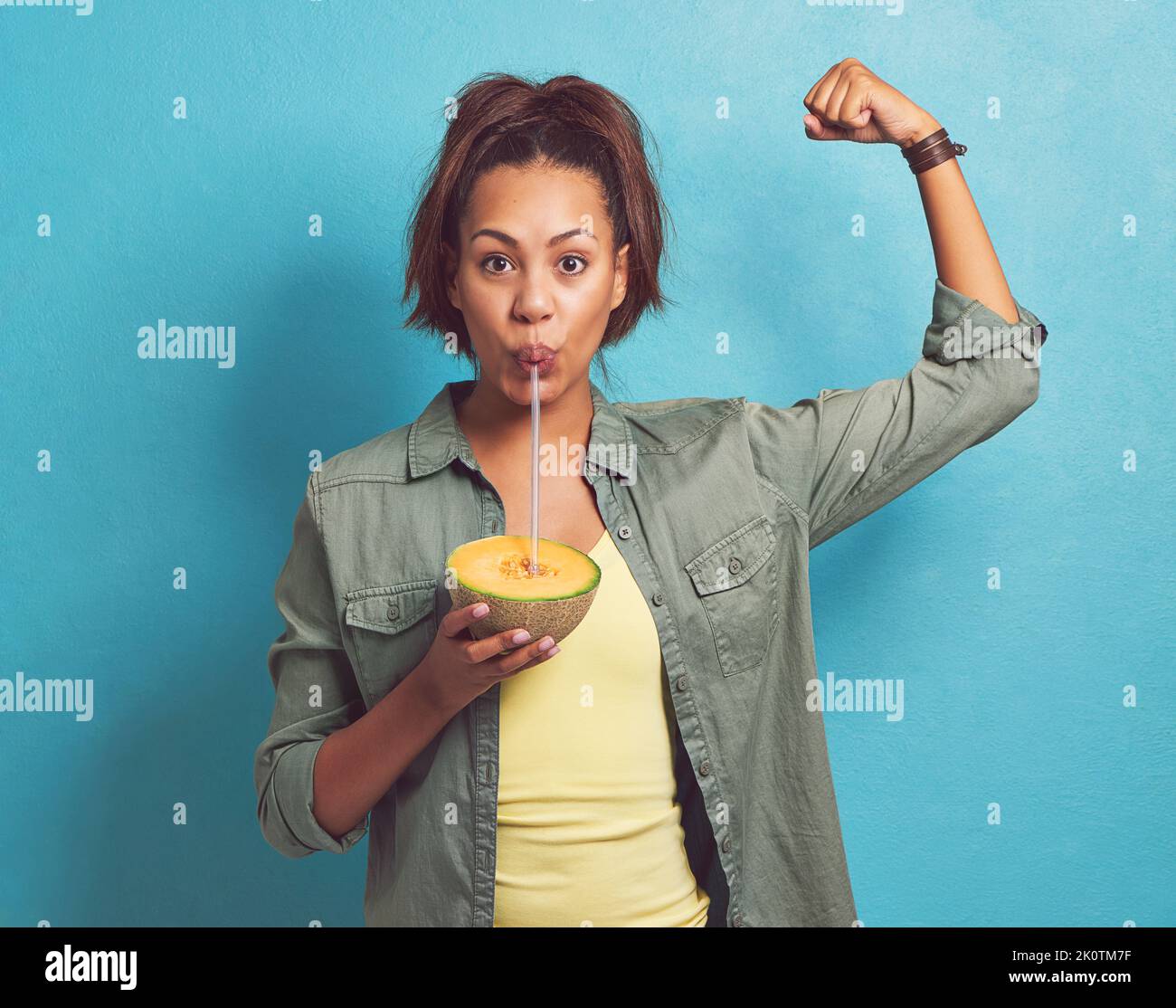 Eine Frau, die sich beugt, während sie auf einer süßen Melone vor blauem Hintergrund nippt. Stockfoto