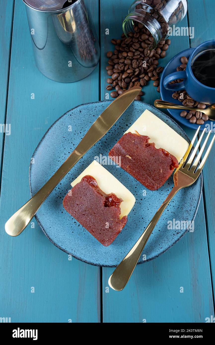 Guava süß mit Käse neben Besteck, Tasse und Kaffeebohnen, auf einem blauen Tisch. Stockfoto