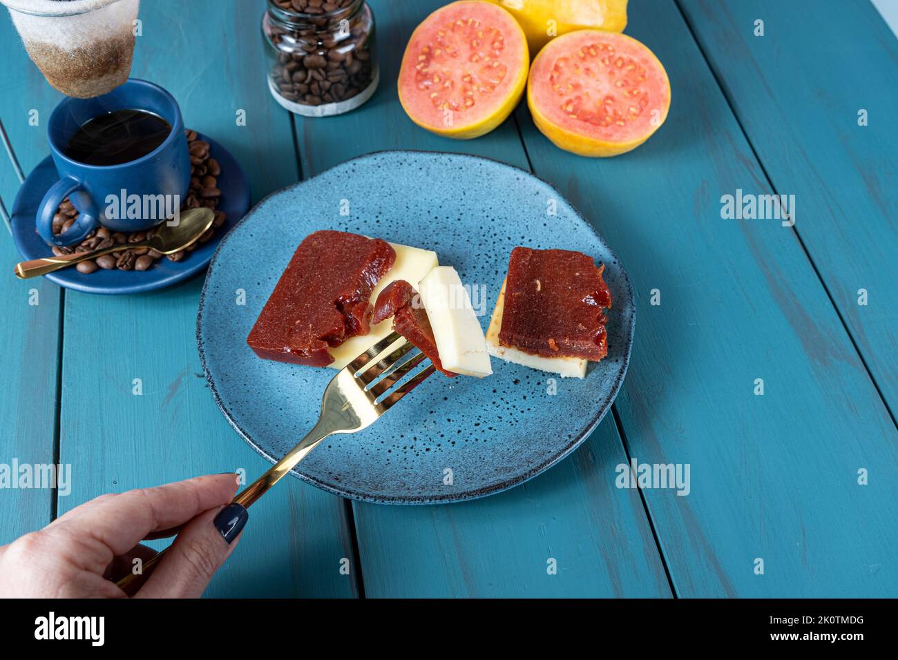 Frau hält mit einer Gabel Stücke von Guava süß mit Käse, umgeben von Bohnen und einer Tasse Kaffee. Stockfoto