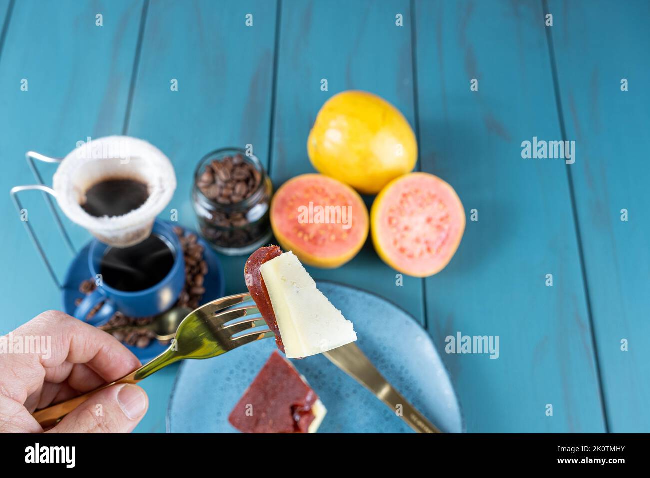 Mann, der eine Gabel mit Guava-Süssstücken mit Käse hält, neben Bohnen und einer Tasse Kaffee. Stockfoto