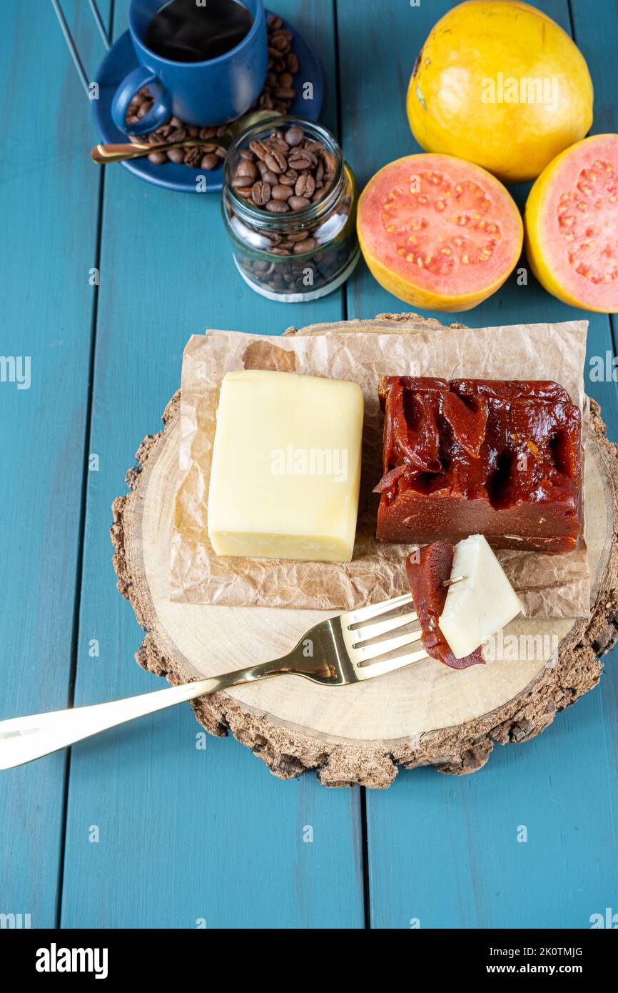 Gabel mit Stücken von Guava süß mit Käse auf einem Holzbrett, neben Bohnen und Tasse Kaffee vertikal. Stockfoto