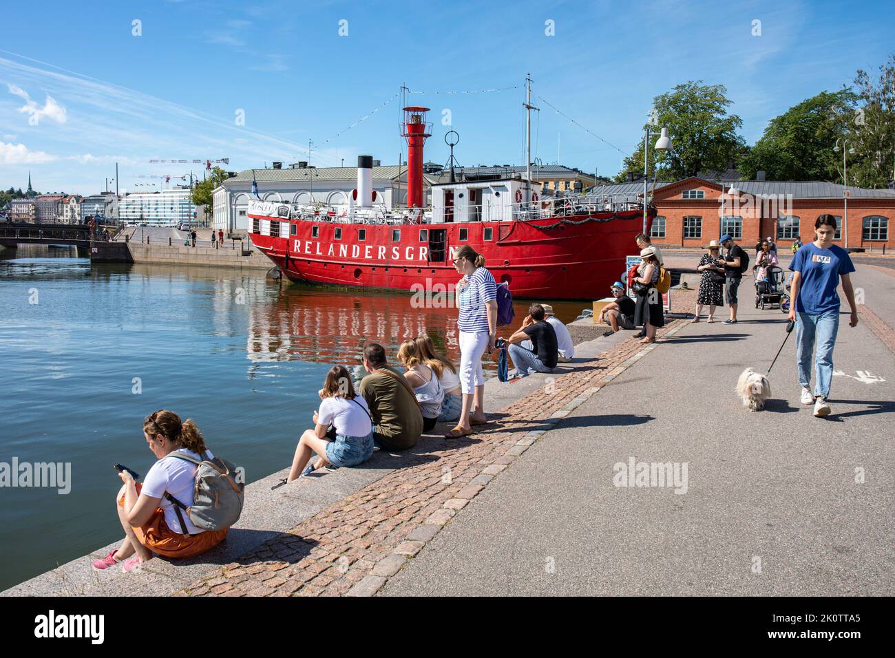 Auf dem Meritullintori-Dock sitzende Menschen warten auf M/S Julia im Bezirk Kruununhaka in Helsinki, Finnland Stockfoto