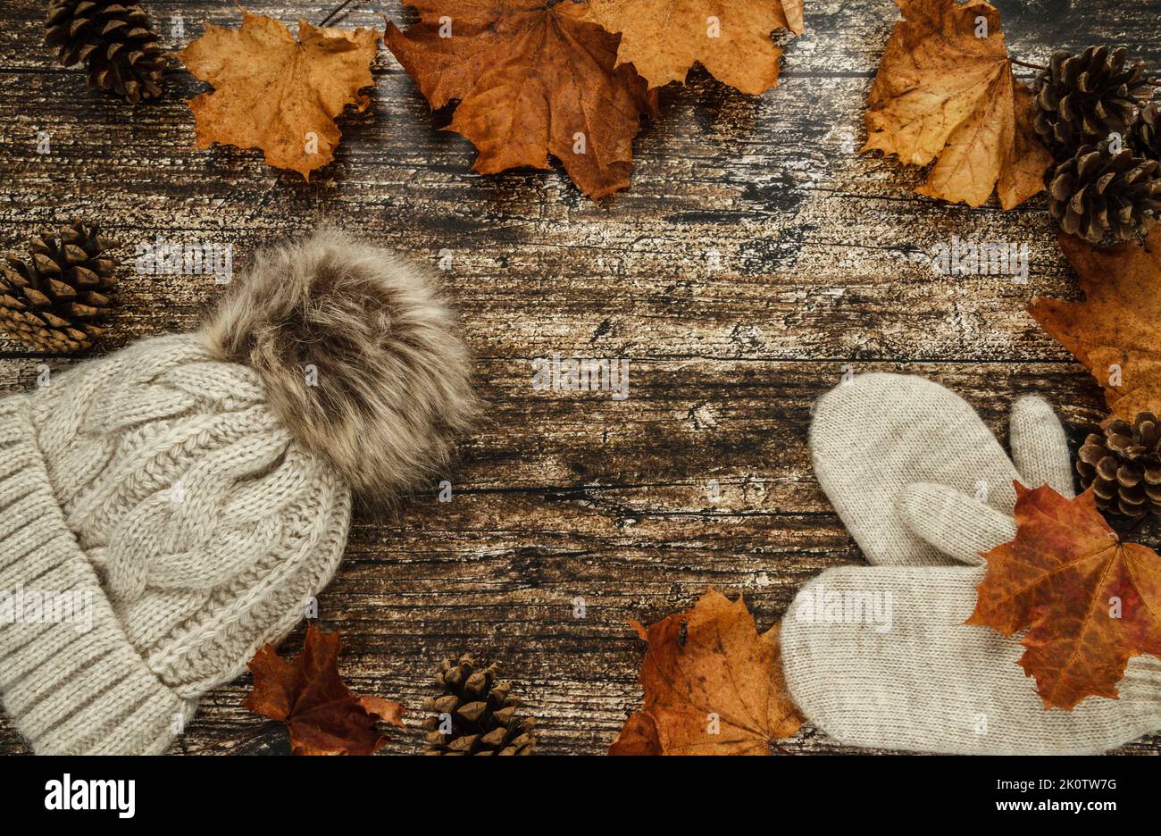 Warme, kuschelige Wintermütze mit Bommel und Handschuhen. Herbst flach Lay Zusammensetzung, mit Kegeln und Herbst Herbstblätter auf Holzgrund. Stockfoto
