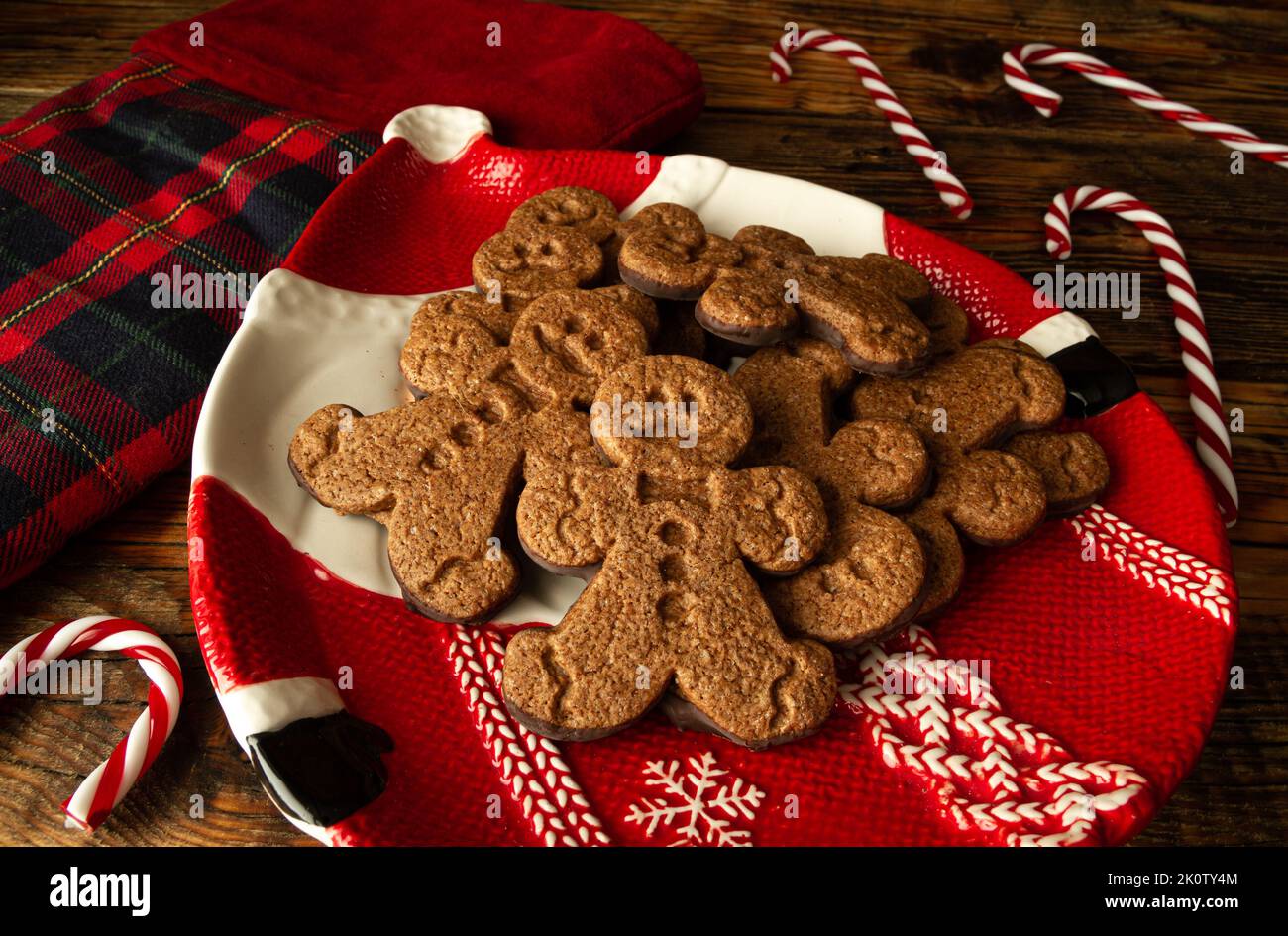 Lebkuchen-Kekse auf einem Teller in Santa-Form, mit Weihnachtsstrumpf und Zuckerstangen. Weihnachtszeit Winterkomposition auf Holzhintergrund. Stockfoto