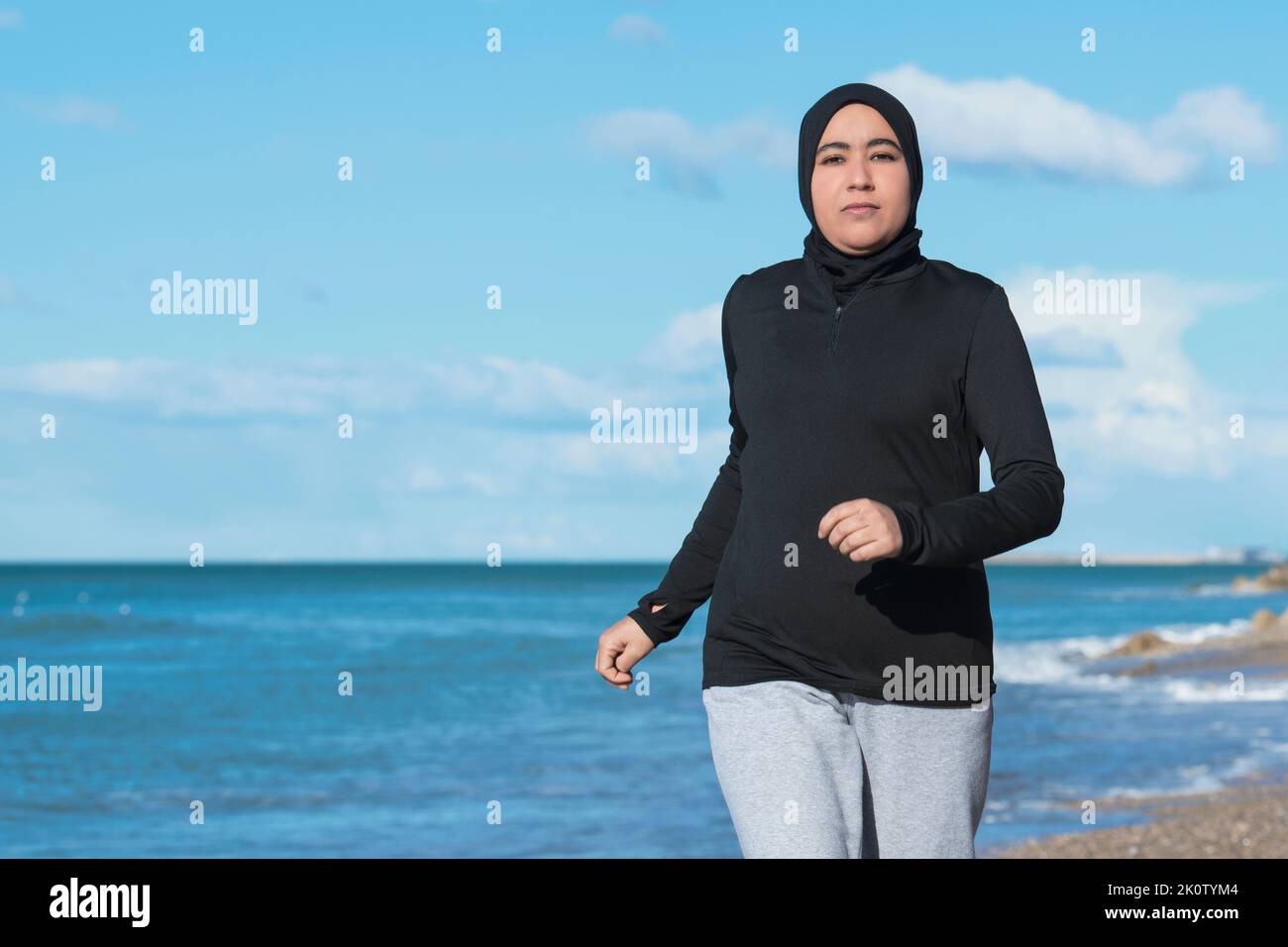 Arabische Frau, die am Strand in der Nähe des Meeres läuft Stockfoto