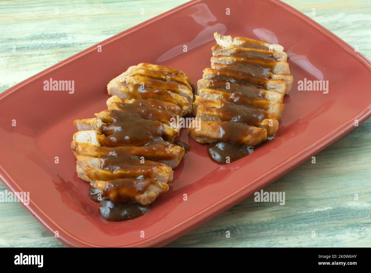 Gegrillte Schweinefiletscheiben mit Hoisin-Sauce auf rotem Servierteller Stockfoto