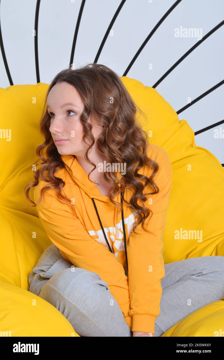 Teenager Mädchen sitzt in einem leuchtend gelben Stuhl und in der gleichen Farbe Kapuzenpullover sie macht Gesichter gekleidet. Hochwertige Fotos Stockfoto