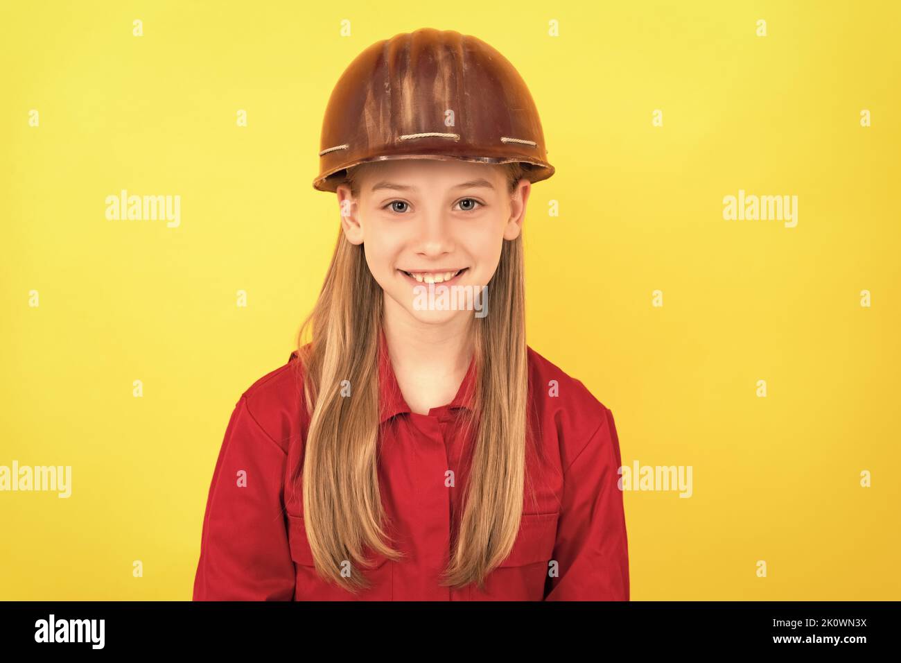 Fröhliches Teenager-Kind im Bauerhelm auf gelbem Hintergrund Stockfoto