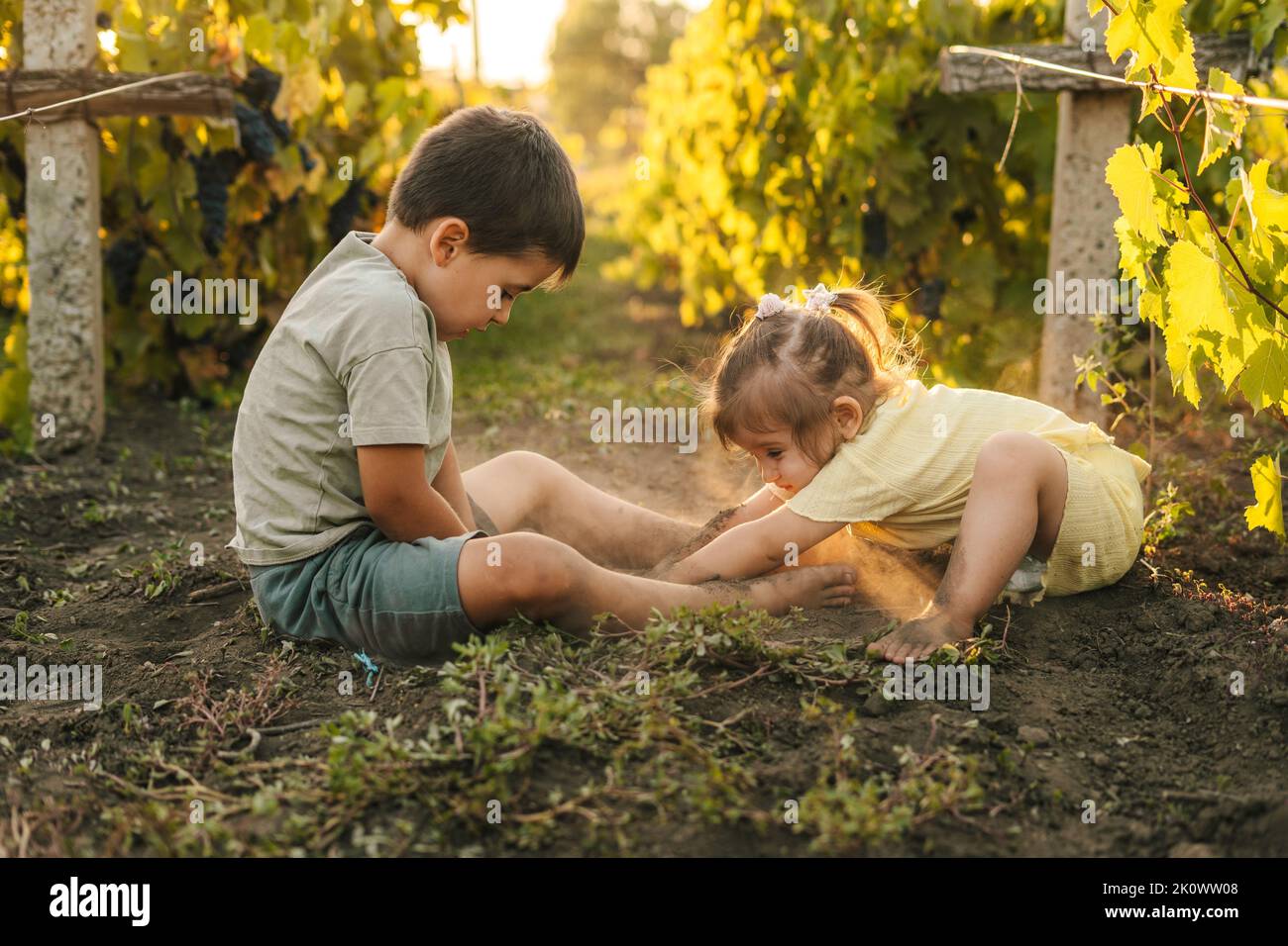 Bruder mit Schwester, die im Weinberg spielt und ein Loch in den Boden gräbt und sich schmutzig gemacht hat. Frohe, liebevolle Familie. Sommerurlaub Aktivitäten. Lustige Familie Stockfoto