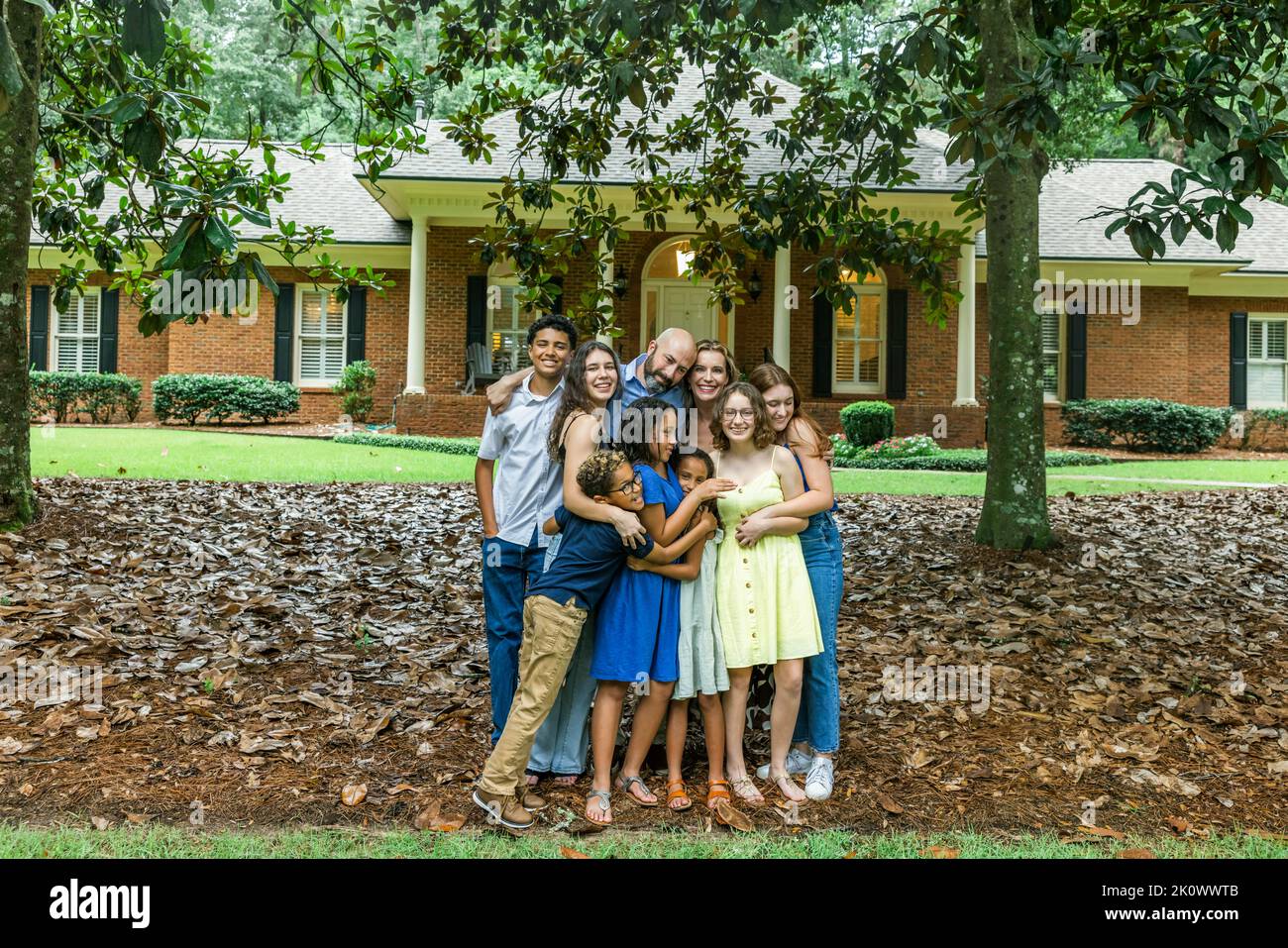Eine große, gemischte und glückliche Familie steht vor ihrem Haus in einer Gruppenumarmung oder Umarmung Stockfoto