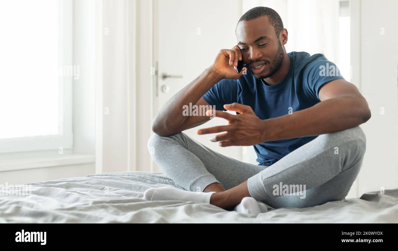 Schwarzer Mann, Der Auf Dem Mobiltelefon Sitzt Und Im Modernen Schlafzimmer Sitzt Stockfoto