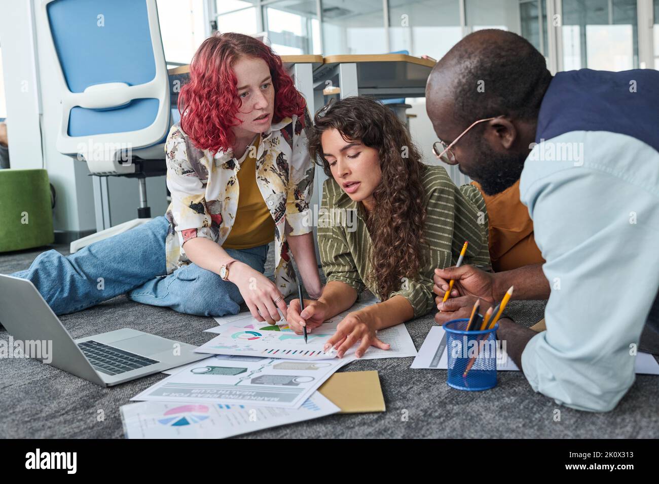 Zwei junge, selbstbewusste Frauen wiesen auf ein Finanzdokument hin, während eine von ihnen den männlichen Kollegen während der Diskussion grafische Daten erklärte Stockfoto