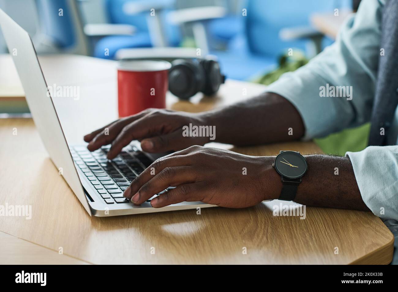 Hände eines jungen afroamerikanischen Geschäftsmannes, der auf dem Laptop-Tastenfeld tippt, während er am Arbeitsplatz im Büro sitzt und nach Online-Daten sucht Stockfoto