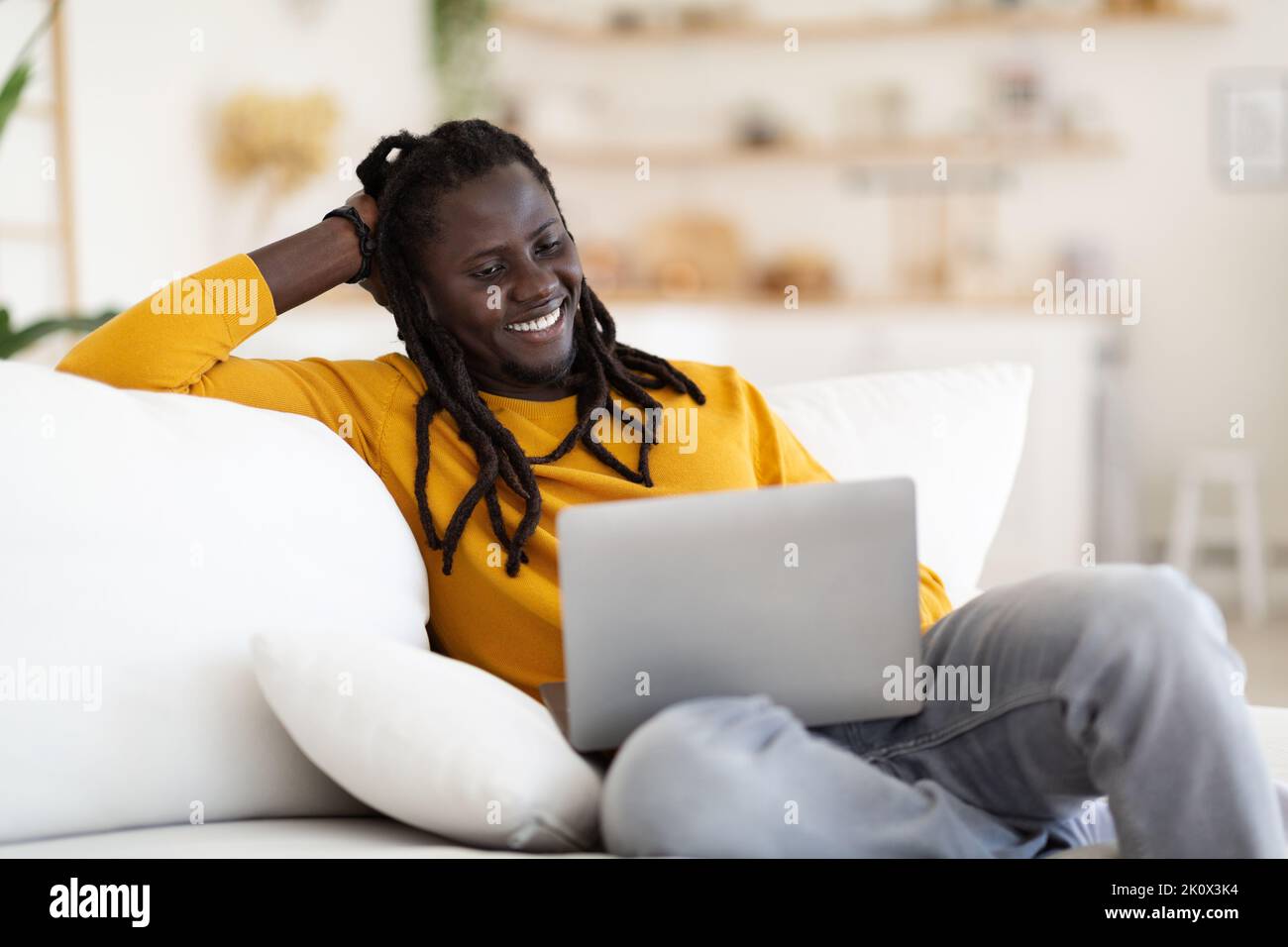 Entspannter schwarzer Mann, der sich zu Hause Filme auf dem Laptop ansieht Stockfoto
