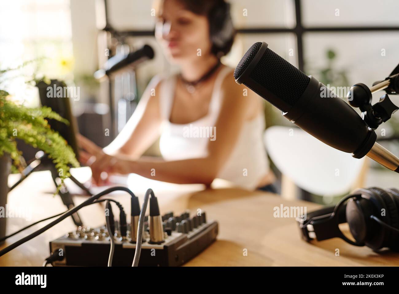 Schwarzes Mikrofon und andere Ausrüstung für die Aufnahme von Audiodateien für Podcasting am Arbeitsplatz des Gastgebers mit Mädchen auf dem Hintergrund Stockfoto