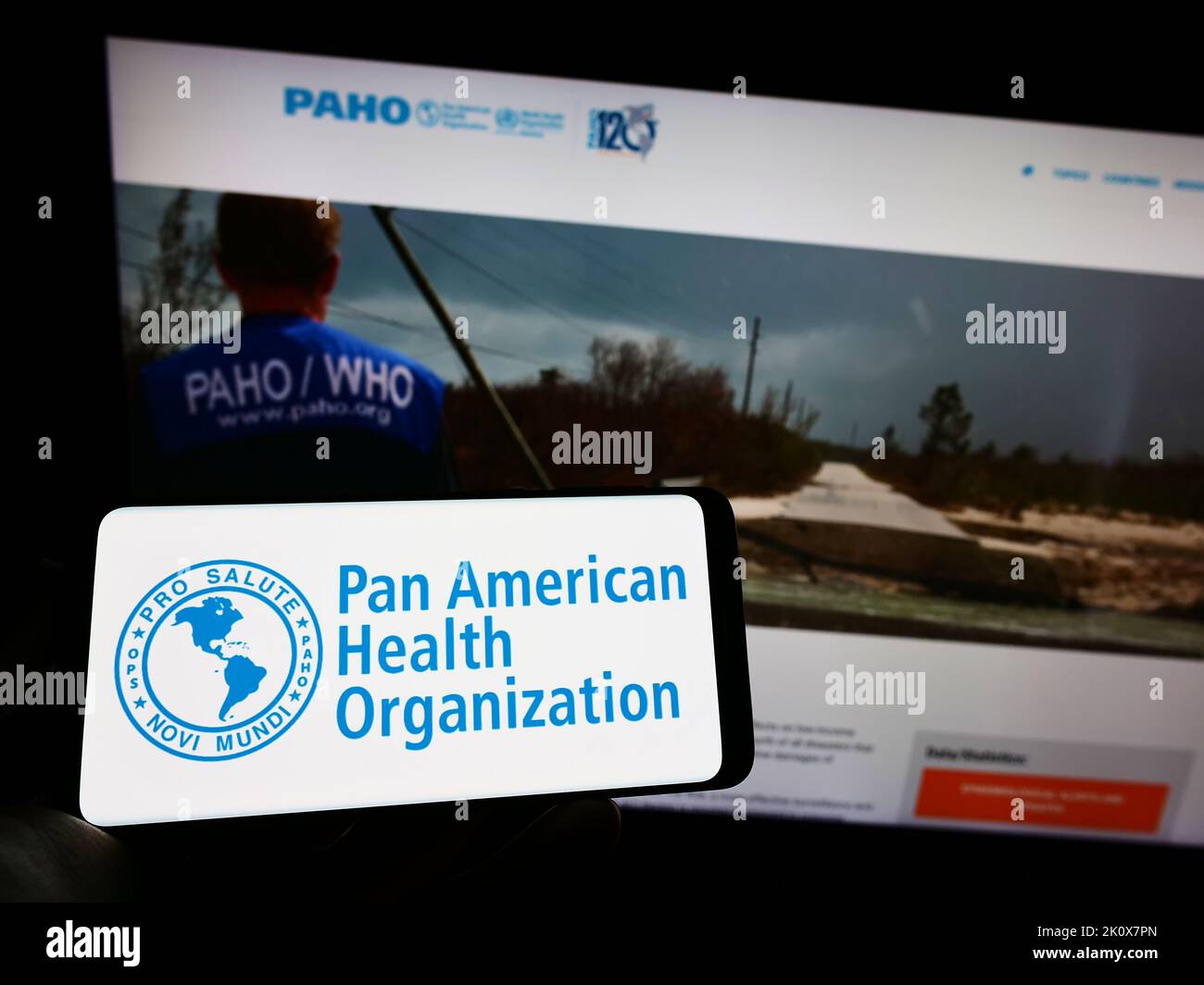 Person mit Mobiltelefon und Logo der Pan American Health Organization (PAHO) auf dem Bildschirm vor der Webseite. Konzentrieren Sie sich auf die Telefonanzeige. Stockfoto