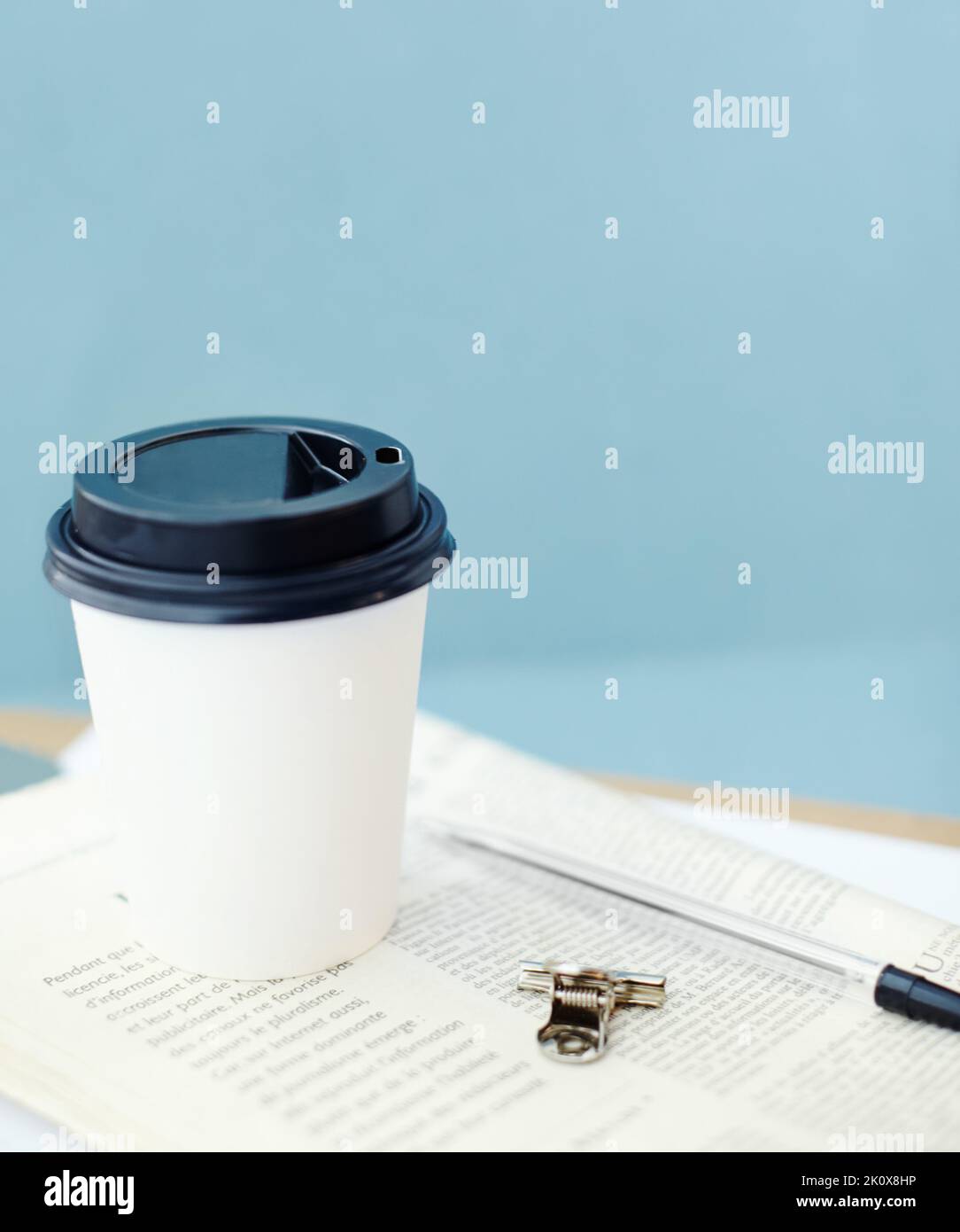 Auf dem Laufenden bleiben bei einer Kaffeepause. Einweg-Kaffeetasse auf einer Zeitung, mit einem Stift und einem Binderclip. Stockfoto