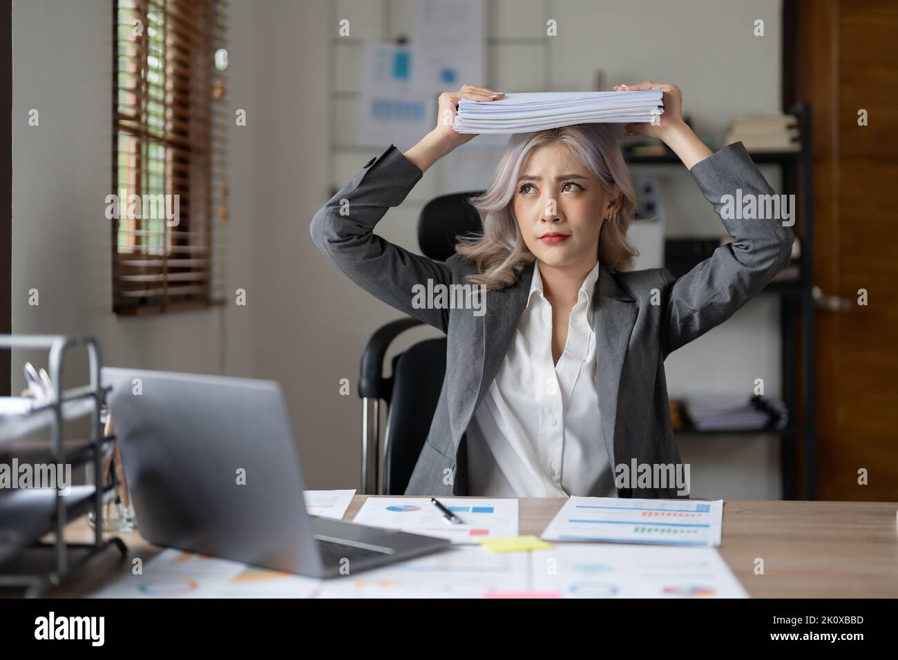 Portrait der schönen asiatischen Frau am Schreibtisch mit Papierkram auf ihrem Kopf. Business überwältigt gestresst Konzept. Stockfoto