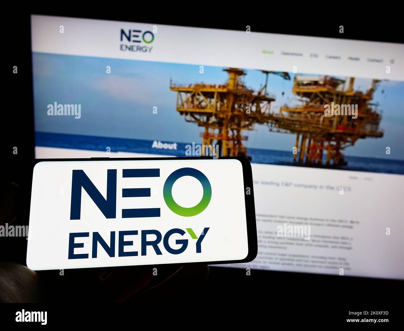 Person, die Mobiltelefon mit dem Logo des britischen Öl- und Gasunternehmens NEO Energy auf dem Bildschirm vor der Business-Webseite hält. Konzentrieren Sie sich auf die Telefonanzeige. Stockfoto