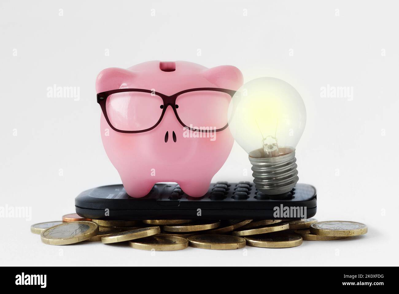 Sparschwein mit Glühbirne auf Rechner und Münzen - Konzept der Strom- und Energieeinsparung Stockfoto