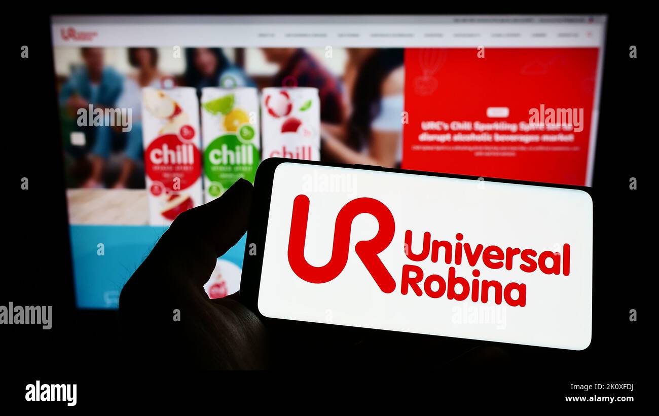 Person, die das Smartphone mit dem Logo der Firma Universal Robina Corporation (URC) auf dem Bildschirm vor der Website hält. Konzentrieren Sie sich auf die Telefonanzeige. Stockfoto