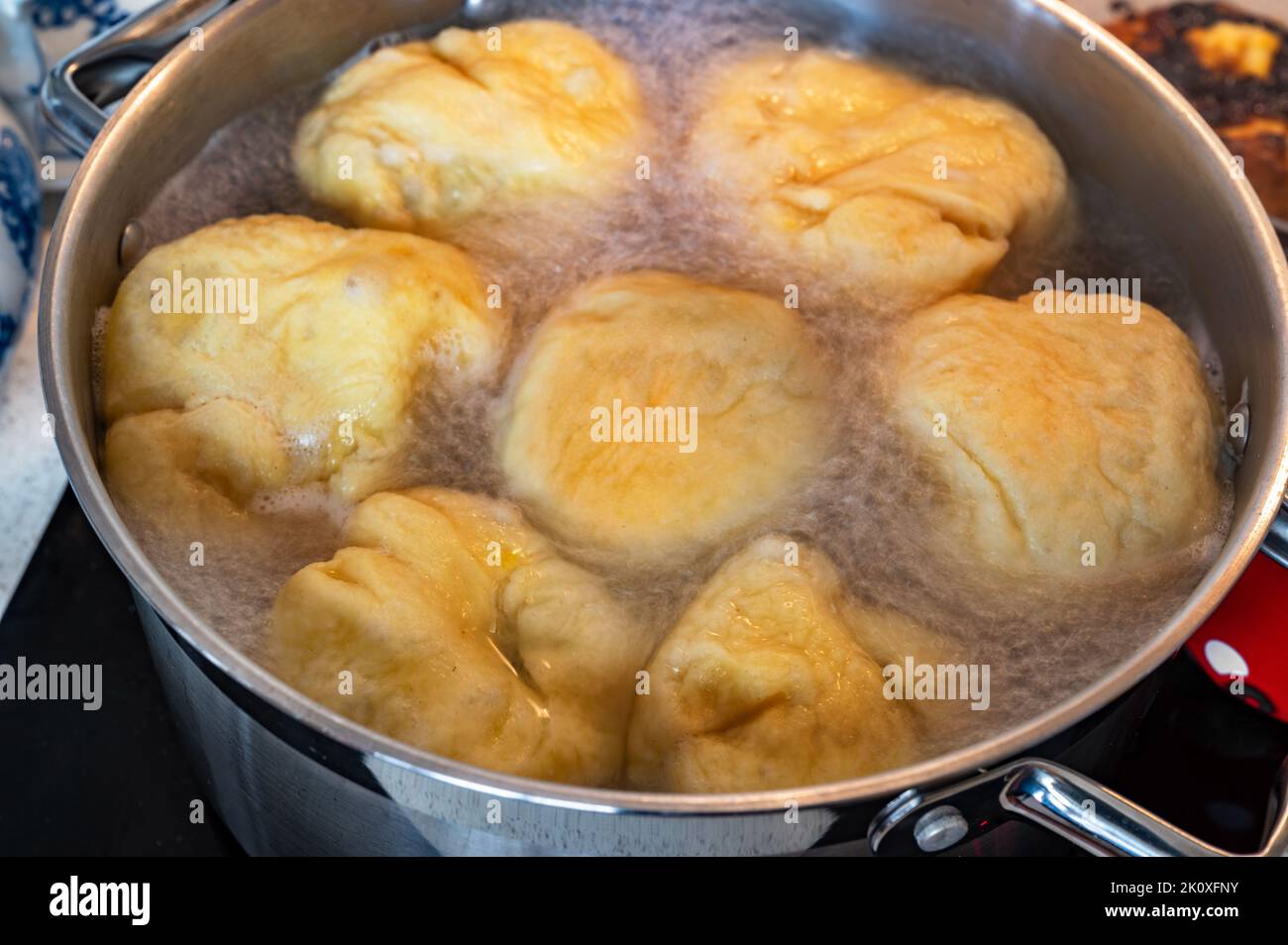 Kochender Knödel im großen Topf. Süße Fruchtknödel, die in kochendem Wasser in einem Topf auf einem Keramikkochfeld schwimmen, Nahaufnahme. Zubereitung von Speisen. Stockfoto