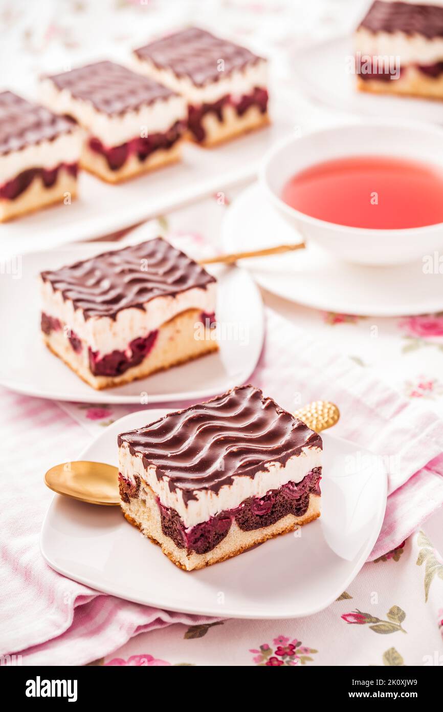 Deutsche Torte Donauwelle - Vanille- und Schokoladenkuchen mit Sauerkirschen, Vanillecreme und Schokoladeneis mit einer Tasse Tee Stockfoto