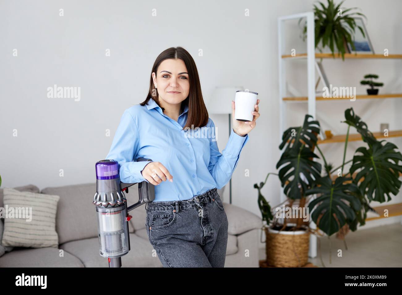 Frau mit Akkumulator-Staubsauger trinkt Kaffee Stockfoto