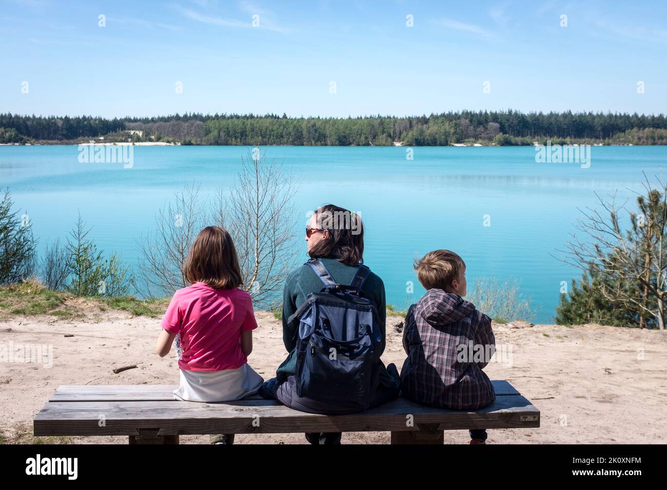 Eine Mutter sitzt mit ihren Kindern auf einer Bank mit Blick auf das auffallend blaue Wasser des Gasselterveld-Sees im Gieten-Borger Forstschutzgebiet, Gasselte, Niederlande. Stockfoto