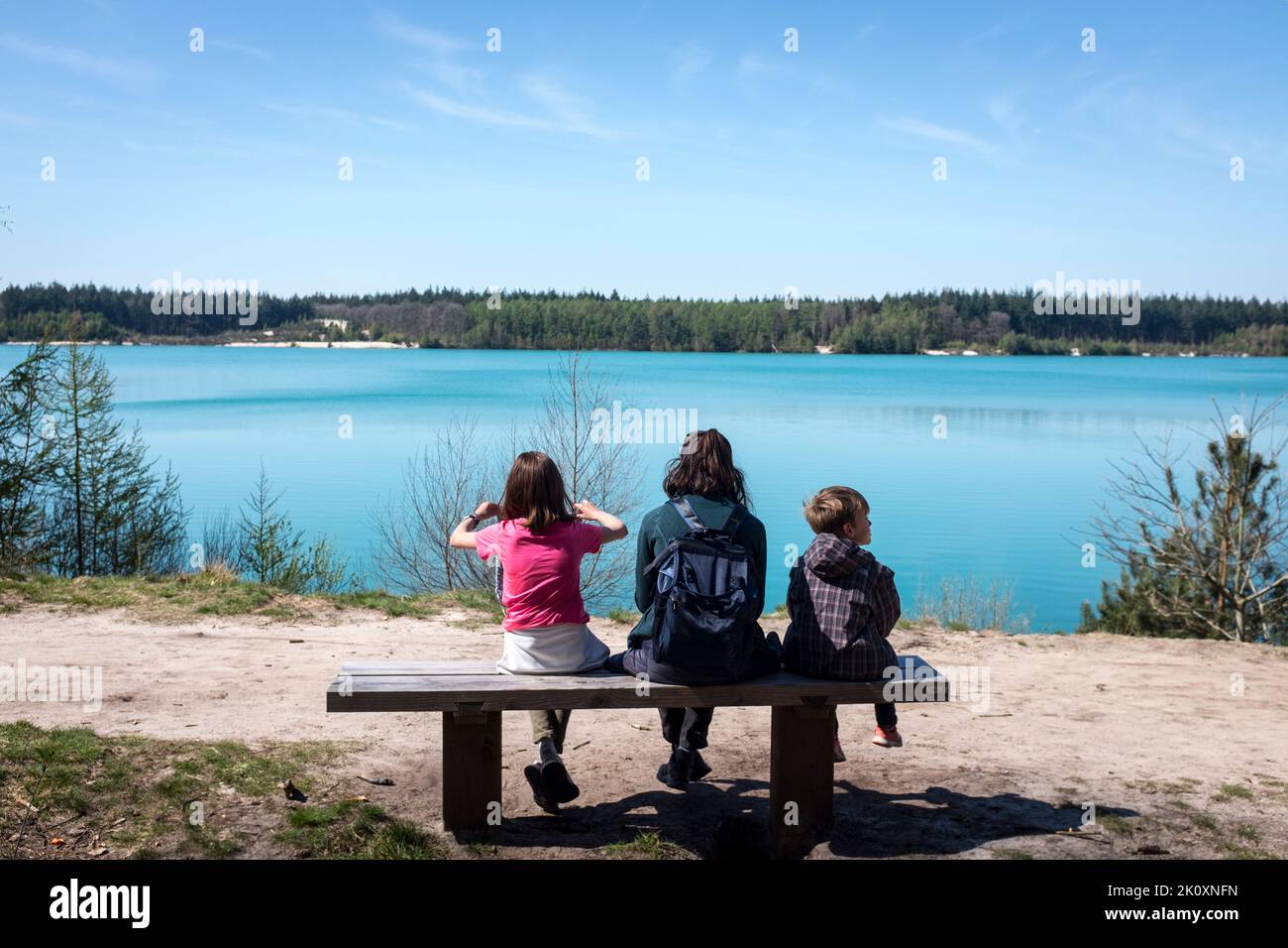Eine Mutter sitzt mit ihrem Sohn und ihrer Tochter auf einer Bank mit Blick auf das auffallend blaue Wasser des Gasselterveld-Sees im Gieten-Borger Forstschutzgebiet, Gasselte, Niederlande. Stockfoto