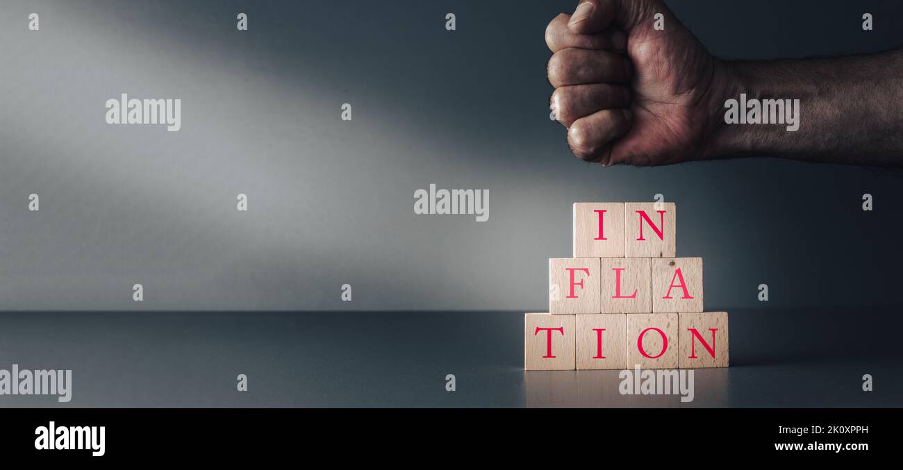 Die Hand versucht, die Inflation zu stoppen oder zu zerquetschen, die Faust kommt auf Holzblöcke auf graublauem Hintergrund, globale Auswirkungen, Rezession. Stockfoto