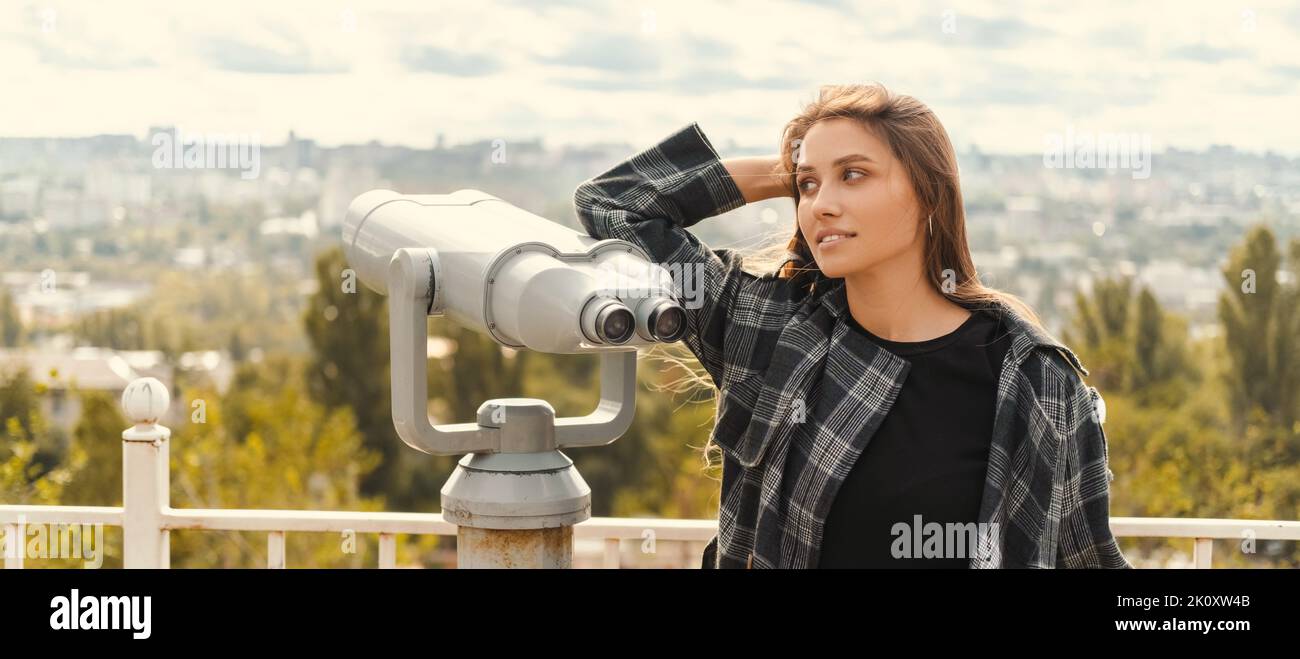 Die junge blonde Frau erkundet eine Stadt mit einem Fernglas vom Beobachtungspunkt im Herbst. Stockfoto