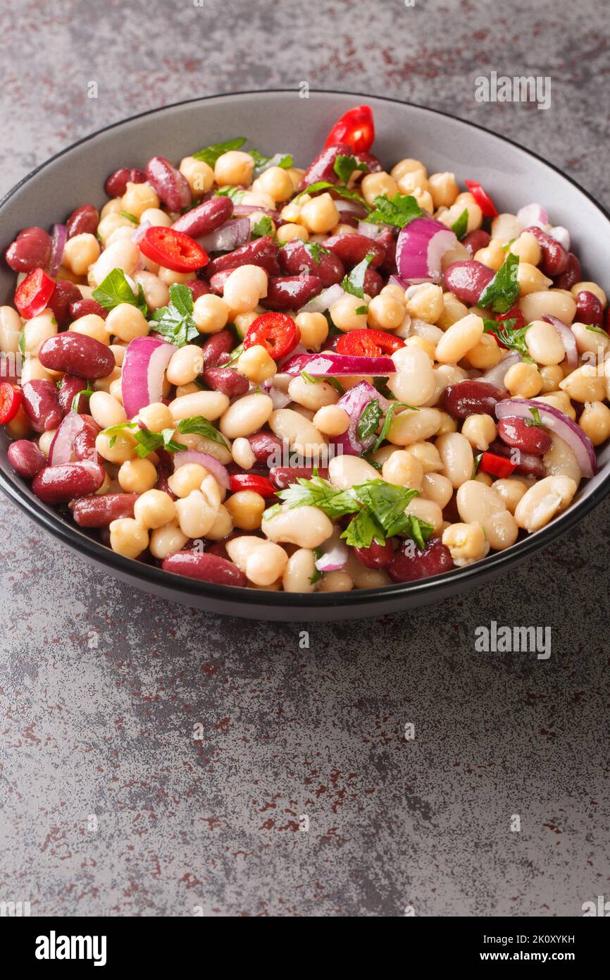 Drei Bohnensalat mit Kichererbsen, Zwiebeln, Chilischoten und Olivenöl-Dressing aus nächster Nähe in einer Schüssel auf dem Tisch. Vertikal Stockfoto
