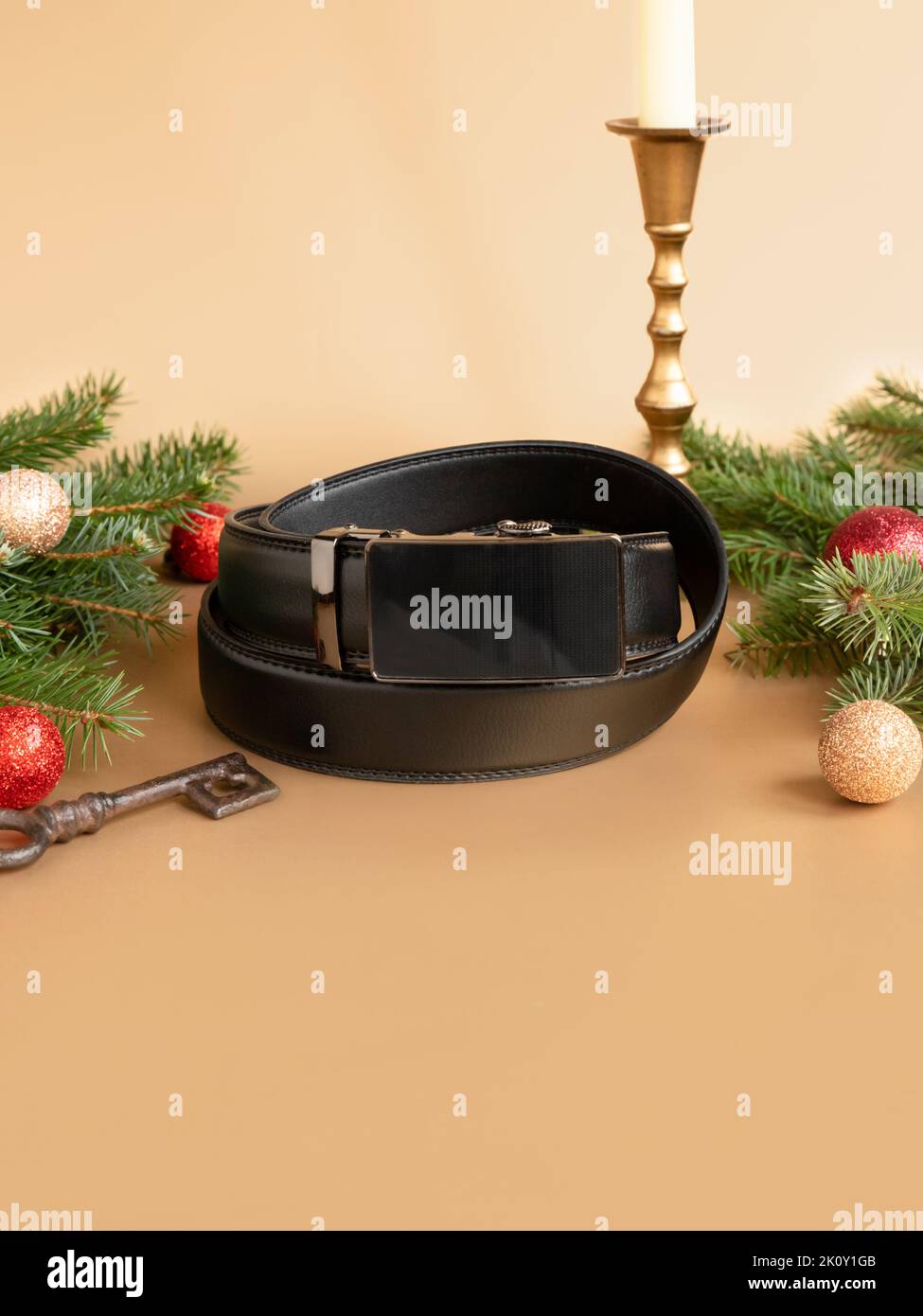 Aufgerollter schwarzer modischer Herren Ledergürtel mit automatischer Schnalle, Weihnachtstanne, glänzenden Kugeln, goldenem Kerzenständer und Schlüssel auf goldenem Hintergrund. Stockfoto