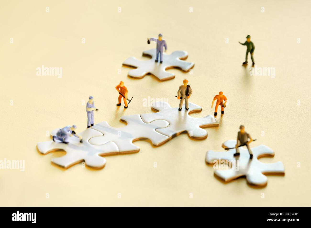 Team von winzigen Arbeiter-Miniaturfiguren auf verbundenen Puzzleteilen auf goldgelbem Papier. Nahaufnahme von weißen Puzzle-Elementen. Stockfoto