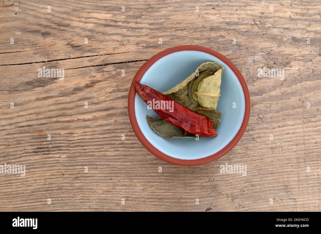 Draufsicht auf Kaffir-Limettenblätter und eine rote Chilischote in einer kleinen Schüssel isoliert auf einem Holzhintergrund. Stockfoto