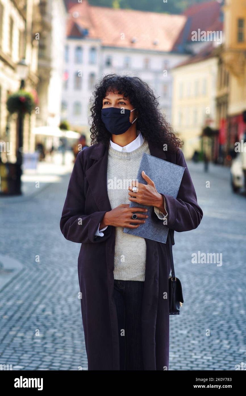 Geschäftsfrau steht auf der Straße mit Gesichtsmaske, die Ordner mit Dokumenten hält Stockfoto