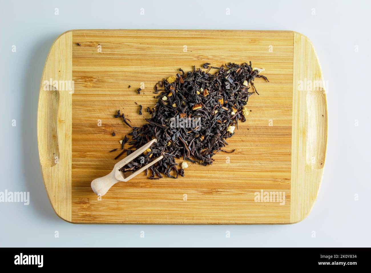 Der Tee ist bereit zum Brühen. Spachtel zum Brühen von Tee. Hintergrund von duftenden schwarzen Teeblättern mit getrockneten Zitrusscheiben und Schalen. Tee auf einem Holzbrett. Stockfoto