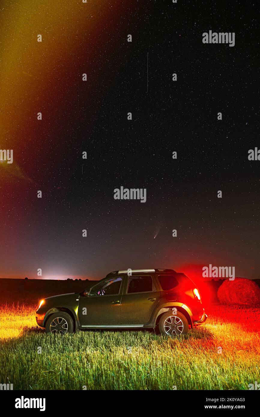 Komet Neowise C2020 F3 in der Nacht Sternenhimmel über Auto-SUV im Sommer Landwirtschaftliche Feldlandschaft. Suv In Der Nacht Sommer Wiese Landschaft Mit Hay Bale Stockfoto