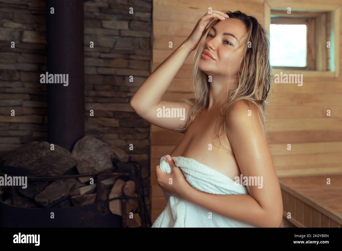 Eine junge Frau entspannt sich und schwitzt in einer heißen Sauna, die in ein Handtuch gehüllt ist. Mädchen in der Sauna. Finnische Sauna im Inneren, klassische Holzsauna mit heißem Dampf Stockfoto