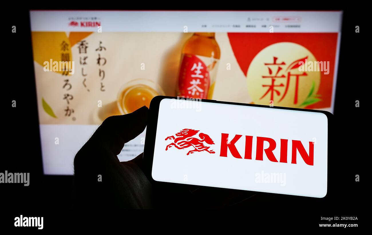 Person, die ein Mobiltelefon mit dem Logo der japanischen Kirin Brewery Company Limited auf dem Bildschirm vor der Business-Webseite hält. Konzentrieren Sie sich auf die Telefonanzeige. Stockfoto