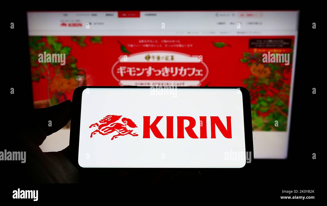 Person mit Mobiltelefon und Logo der japanischen Kirin Brewery Company Limited auf dem Bildschirm vor der Business-Webseite. Konzentrieren Sie sich auf die Telefonanzeige. Stockfoto