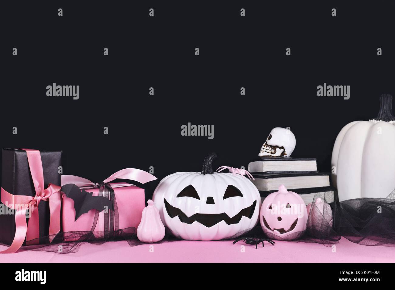Pink-weißes Halloween Dekor mit schwarzen und weißen Kürbissen, Zauberbüchern und Spinnen auf schwarzem Hintergrund mit Kopierfläche Stockfoto