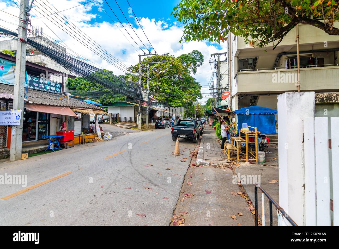 CHIANG MAI, THAILAND - 4.11.2019: Straße in der Stadt Chiang Mai. Blick auf die Straße mit Autos, Holzhäusern, Bäumen. Schmale Straße in der Mitte. Stockfoto