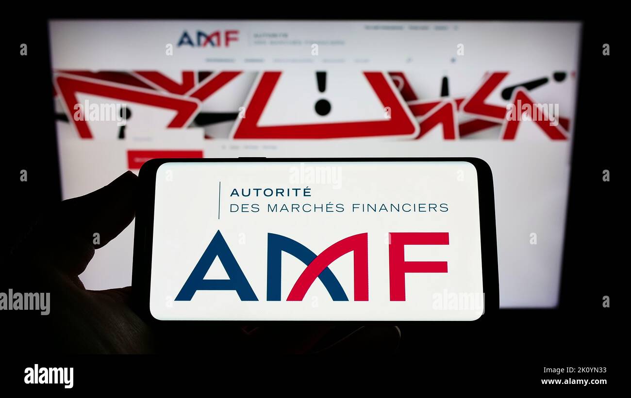 Person, die ein Mobiltelefon mit dem Logo der Regulierungsbehörde Autorite des Marken Financiers (AMF) auf dem Bildschirm vor der Webseite hält. Konzentrieren Sie sich auf die Telefonanzeige. Stockfoto Person, die ein Mobiltelefon mit dem Logo der Regulierungsbehörde Autorite des Marken Financiers (AMF) auf dem Bildschirm vor der Webseite hält. Konzentrieren Sie sich auf die Telefonanzeige. Stockfoto